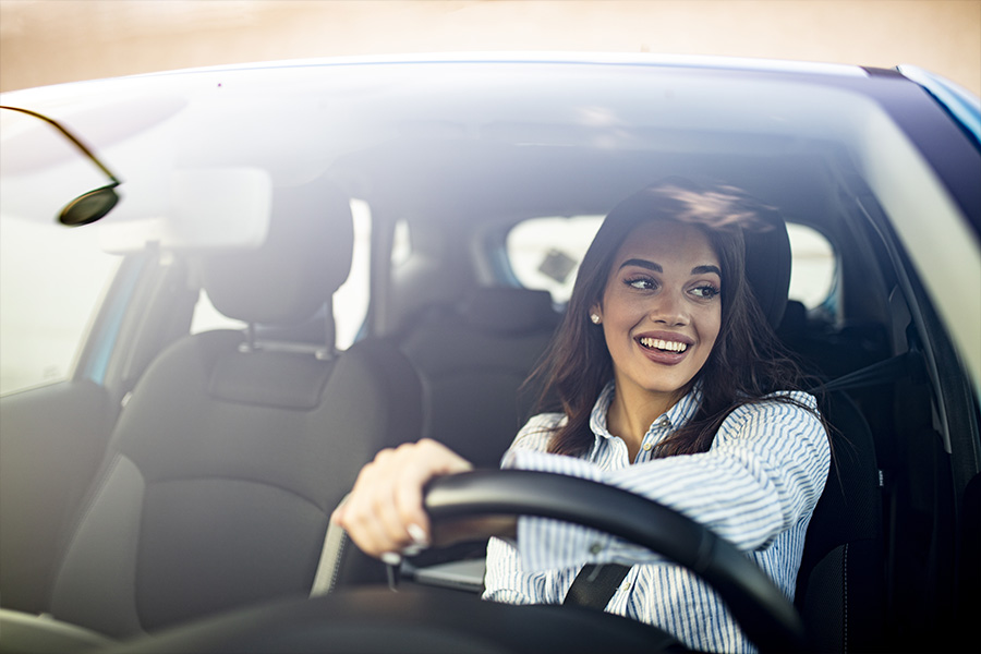 Blog - Woman Smiling While Turning in Her Car as She is Driving and Looks Out the Window on a Nice Day